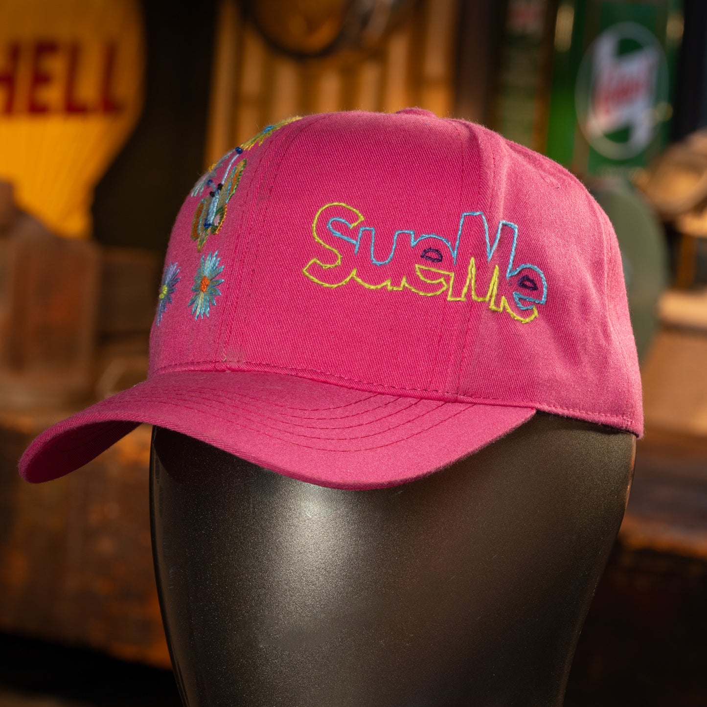 Pink cap with colorful text and designs on a mannequin head against a blurred background.