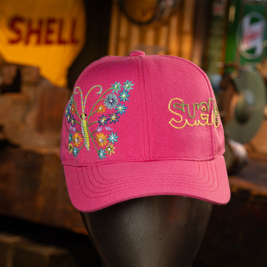Pink cap with butterfly and floral design on a mannequin head, with blurred background