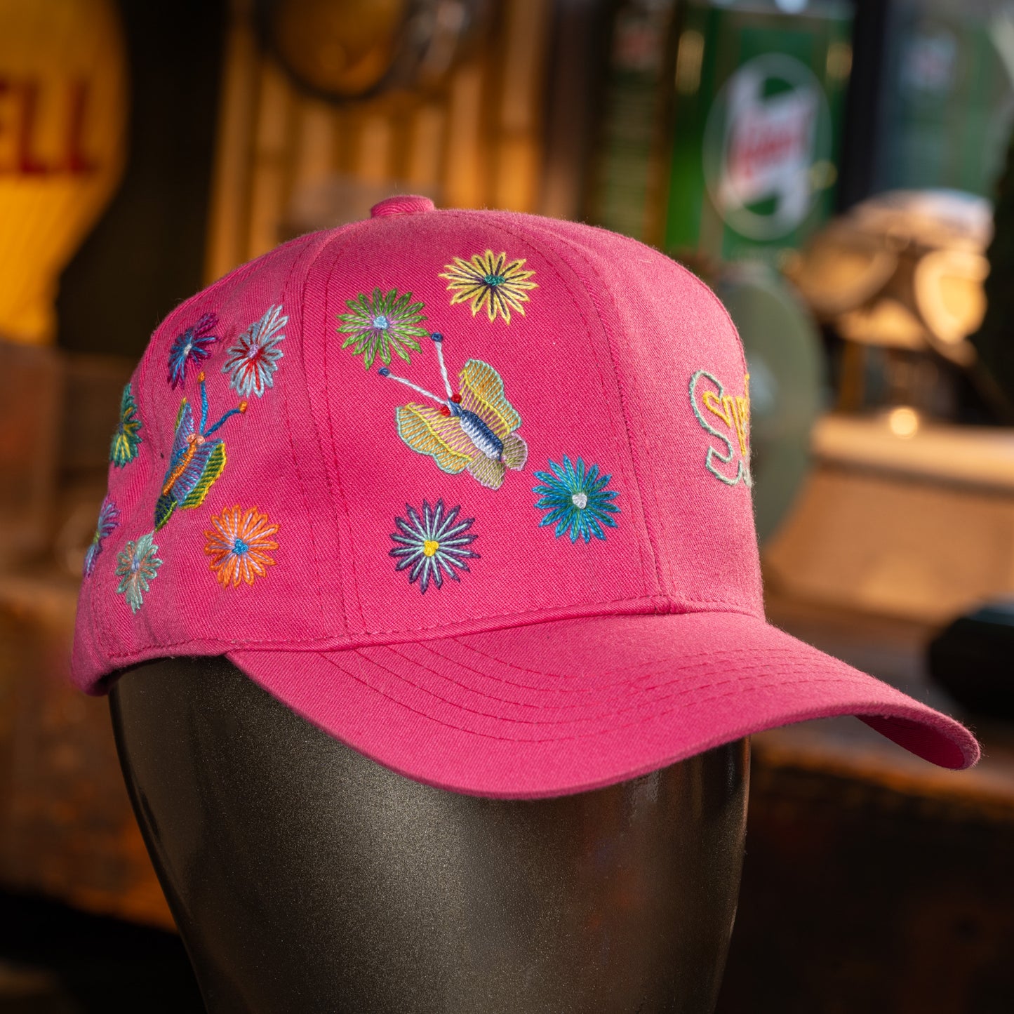 Pink cap with colorful floral and butterfly embroidery on a mannequin head, blurred background