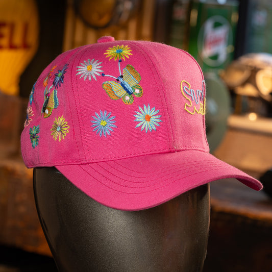Pink cap with colorful butterfly and flower designs on a mannequin head against a blurred background.
