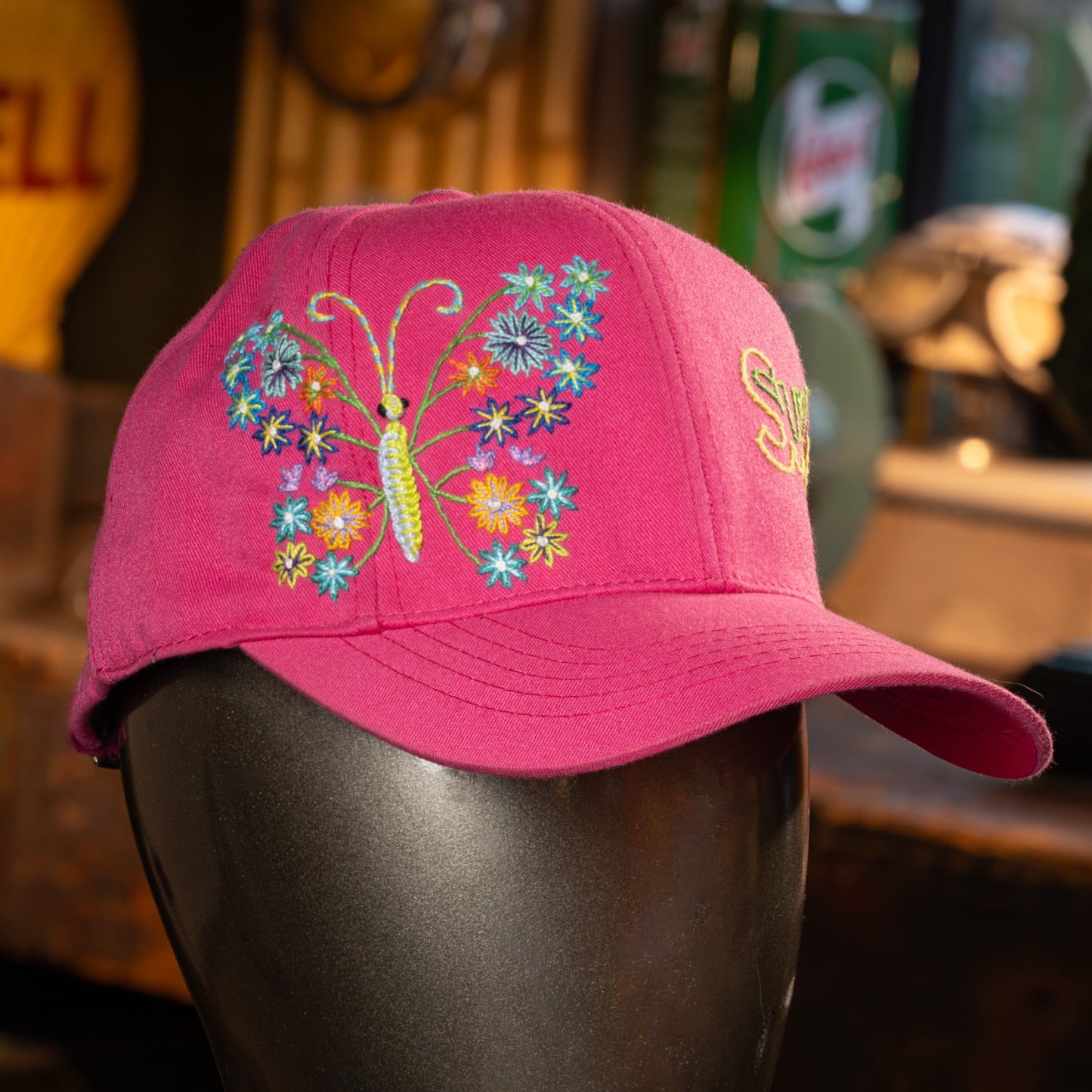 Pink cap with butterfly and floral design on a mannequin head against a blurred background