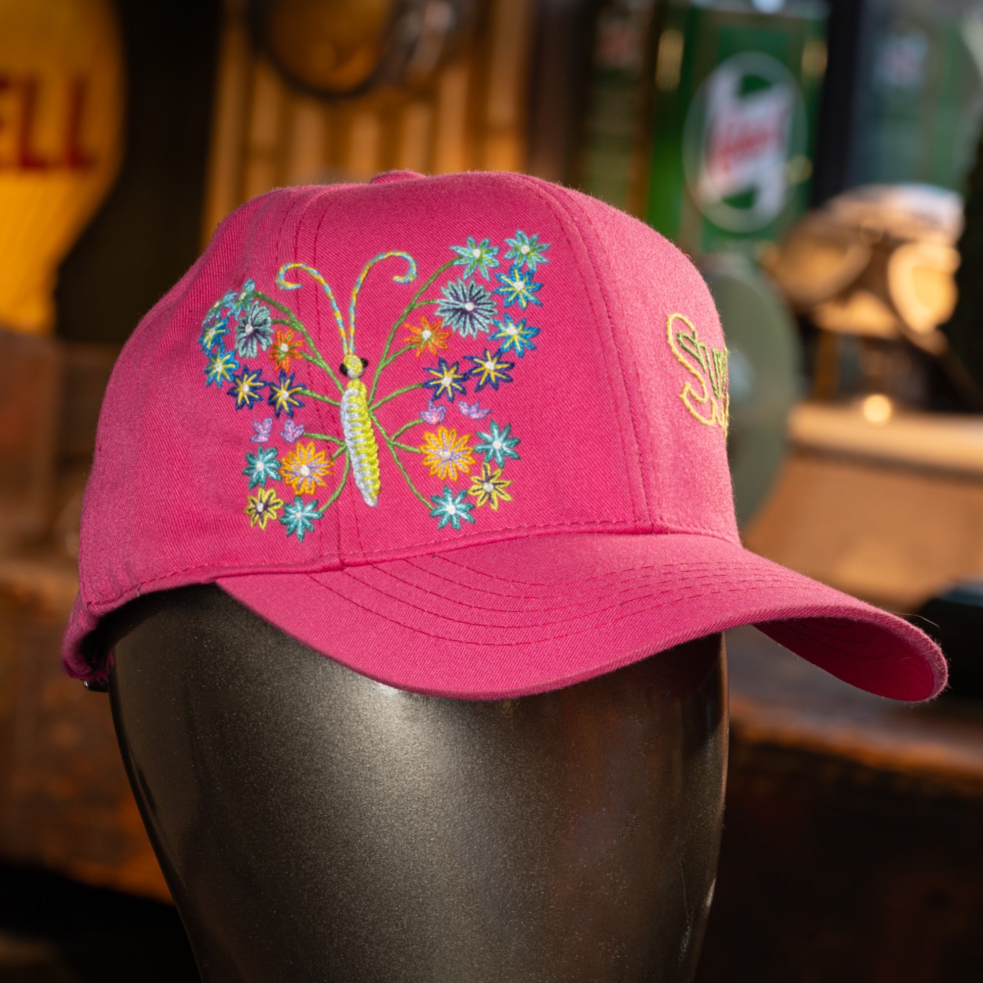 Pink cap with butterfly and floral design on a mannequin head against a blurred background
