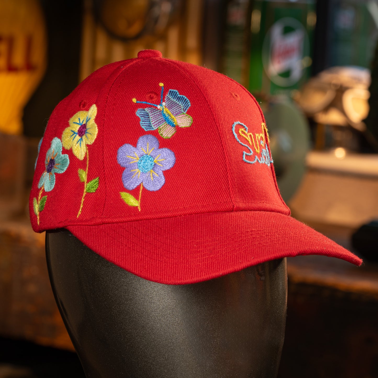 Red cap with floral designs on a mannequin head against a blurred background