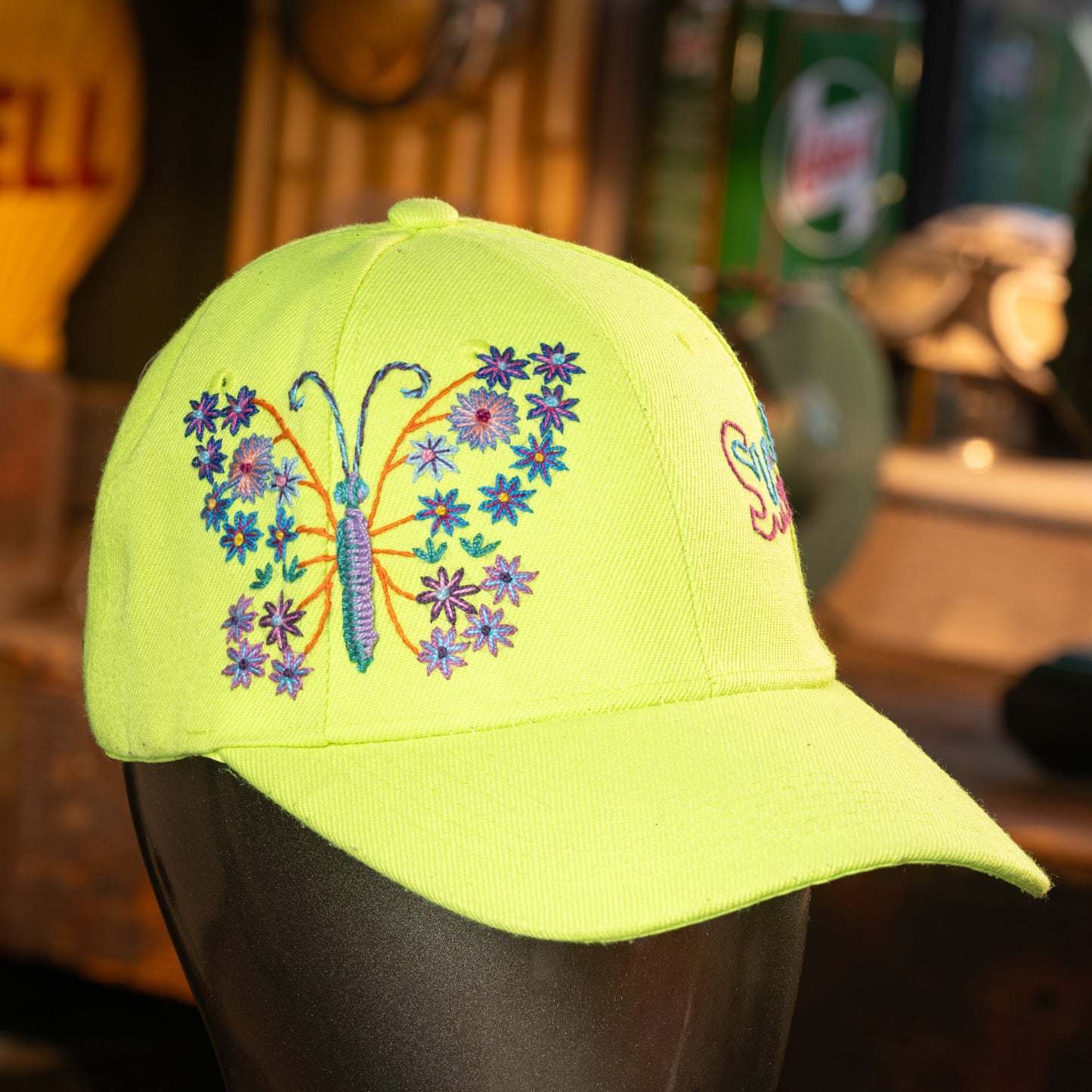 Yellow cap with butterfly and floral design on a mannequin head, blurred background