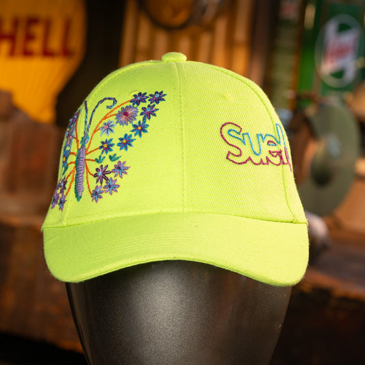 Neon green cap with floral design and 'SueMe' text on a mannequin head against a blurred background.