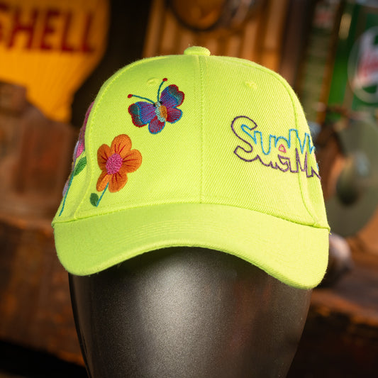 Lime green cap with butterfly and flower designs on a mannequin head against a blurred background.