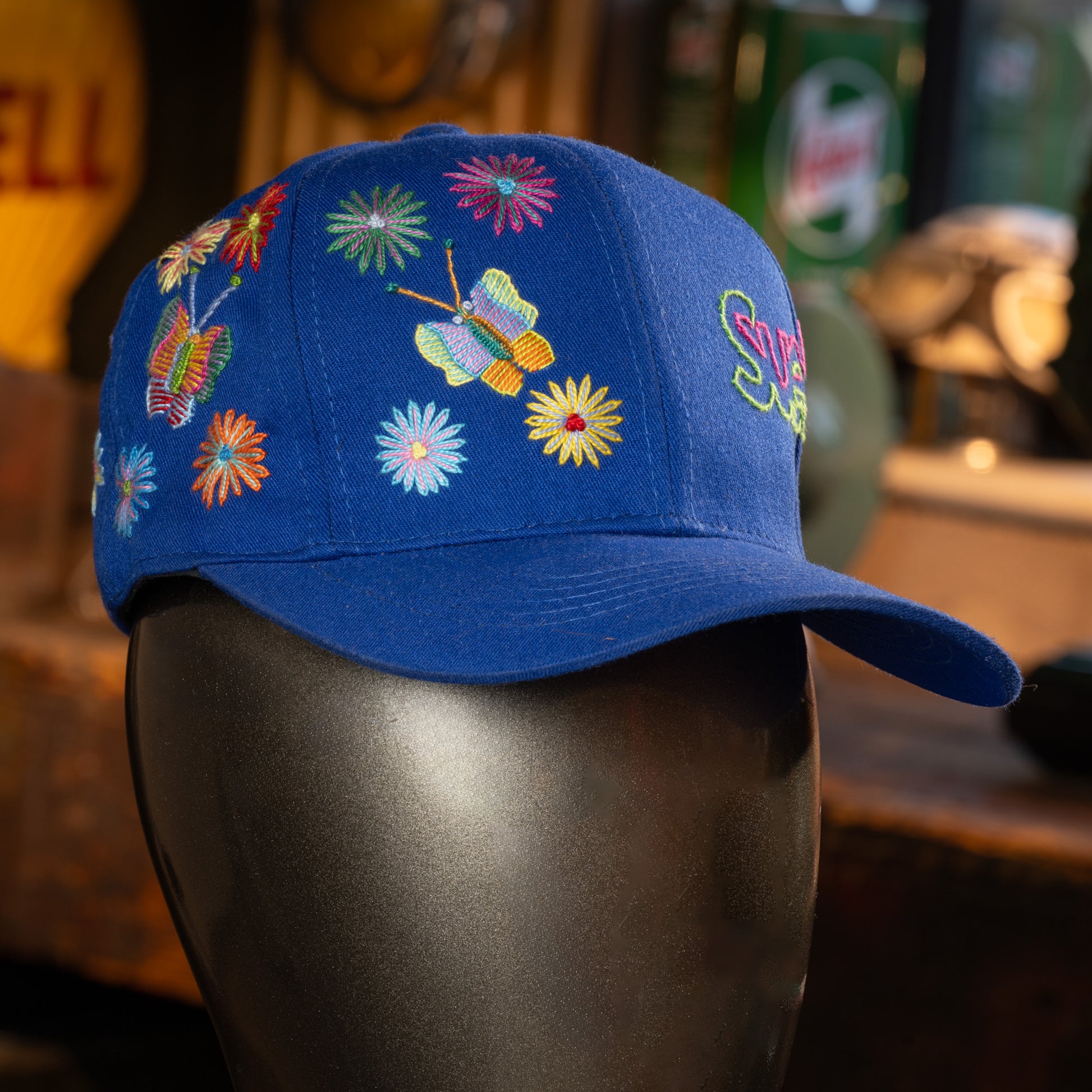 Blue cap with colorful floral and butterfly embroidery on a mannequin head.
